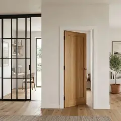 Une porte en bois clair est ouverte, révélant un salon lumineux. Une autre porte grise est visible à gauche, près d'une verrière industrielle.