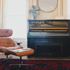 A brown leather armchair and ottoman, a mismatched pair, sit on a Persian rug next to an antique piano.