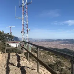 Vista panorámica desde la sierra del Carche, con una cabaña de madera, antena de comunicaciones y un paisaje de campos y montañas.