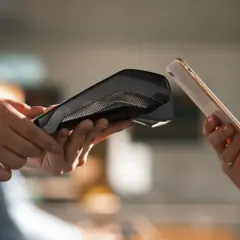 Dwie dłonie zbliżają do siebie telefon i terminal płatniczy. Pokazuje to, jak placic telefonem w prosty i szybki sposób.