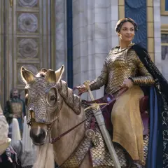 En kvinna i gyllene rustning rider en häst med en imponerande rustning. Scenen är från sagan om ringen serie.