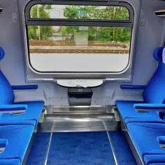 Wnętrze wagonu Intercity z niebieskimi siedzeniami i oknem z widokiem na tory.