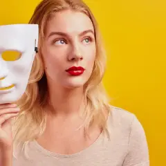 Blondynka z czerwoną szminką trzyma białą maskę, zastanawiając się nad hipokryzją.