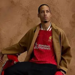 Mężczyzna w brązowej marynarce i czerwonej koszulce Liverpool z logo Standard Chartered.