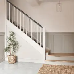 Elegancka klatka schodowa z angielską boazerią, ozdobiona rośliną w wiklinowym koszu i dywanem z juty.