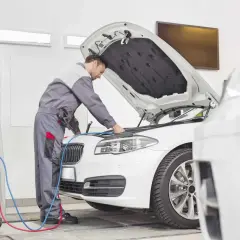 Mechanik sprawdza silnik białego BMW. Zastanawiasz się, ile teraz kosztuje przegląd samochodu?