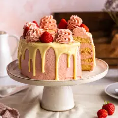 Eine wunderschöne Erdbeertorte, perfekt für jedes Erdbeertorte rezept. Mit rosa Buttercreme, weißen Schokoladenglasur-Tropfen und frischen Erdbeeren dekoriert.