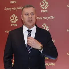 Prezes PZPN w garniturze, poprawiający krawat. Tło ozdobione logotypami PZPN i hasłem "Łączy nas piłka".