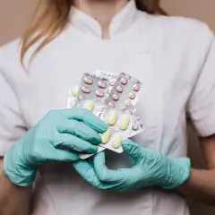 Farmaceuta w rękawiczkach trzyma kilka opakowań tabletek.