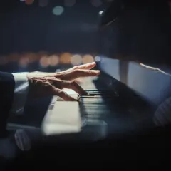 Dłoń pianisty grająca nokturn na fortepianie, w tle rozmyte światła.