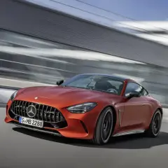 Pomarańczowy Mercedes-AMG GT 63 S pędzi po drodze, za nim rozmyte tło nowoczesnej architektury.