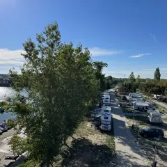 Słoneczny dzień na kempingu w Dunajskiej Stredzie. Przy jeziorze stoją kampery, a na wodzie widać dmuchane atrakcje i łódki.