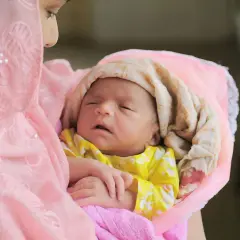 Une mère câline son nouveau-né, enveloppé dans des tissus roses et crème. Une douce image pour des douces félicitations naissance islam.