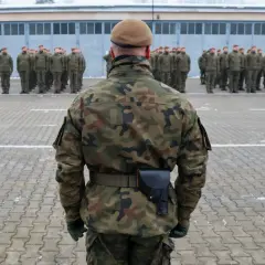 Żołnierze w mundurach polowych stoją na placu apelowym. W tle budynek koszar. To może być początek obowiązkowej służby wojskowej.