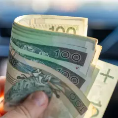 Dłoń trzyma zwitek polskich banknotów 100 zł. To może być wsparcie z ZUS, świadczenie wspierające dla potrzebujących.