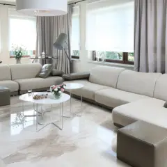 Nowoczesne aranżacje salonu z dużym oknem. Jasne sofy, błyszcząca podłoga i eleganckie zasłony tworzą przytulną atmosferę.