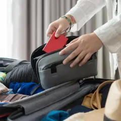 Pakowanie na długi weekend. Czerwony paszport trafia do kosmetyczki, obok ubrań i kapelusza.