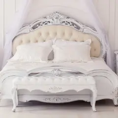 Elegancka sypialnia w stylu francuskim, z białym, rzeźbionym łóżkiem, baldachimem i ozdobnymi szafkami nocnymi.