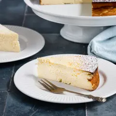 Ein Stück cremiger Quarkkuchen ohne Boden, bestäubt mit Puderzucker, wartet auf dem Teller.