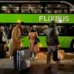 Ludzie z bagażem czekają na zielonego Flixbusa.