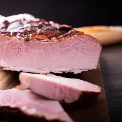 Pokrojona, wędzona szynka na desce. Idealna do przygotowania pysznych kanapek, a jej smak zachwyci każdego, kto lubi wiedzieć, jak parzyć szynkę.