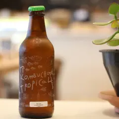 Brązowa butelka kombuchy z zieloną zakrętką i etykietą "Kombucha Tropical".