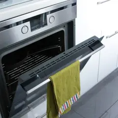 Otwarty piekarnik z zielonym ręcznikiem na drzwiczkach. W środku ruszt i naczynie. Gotowy do czyszczenia przez pyrolizę w piekarniku.