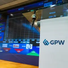 Stojak z mikrofonem przed ekranem z wykresem giełdowym GPW.