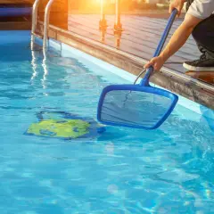 Mann reinigt den Pool mit einem Kescher. Ein gelbes Spielzeug schwimmt im klaren Wasser.
