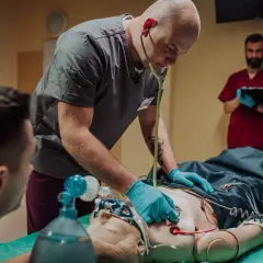Ratownik medyczny ćwiczy resuscytację na fantomie, używając stetoskopu i maski tlenowej.