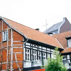 Urokliwy dom szachulcowy z ceglanymi ścianami i białymi belkami, otoczony innymi budynkami.