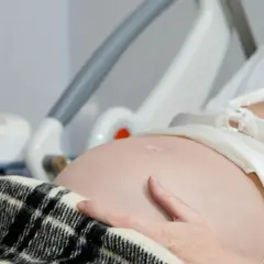 Kobieta w szpitalnym łóżku, z ręką na brzuchu, czeka na poród. Obok monitor KTG, który pomaga ocenić stan dziecka i może sugerować, jak przyspieszyć poród.