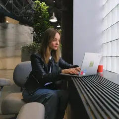 Kobieta siedzi przy laptopie, ucząc się, jak założyć konto na OLX. W tle nowoczesne wnętrze z roślinami.