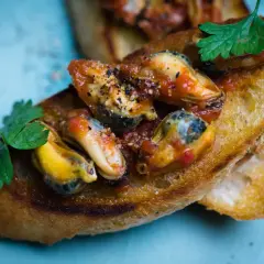 Chrupiące grzanki z soczystymi mule w pomidorach, ozdobione natką pietruszki. Pyszna przekąska.