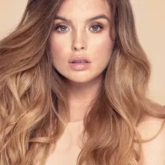 Mujer con cabello largo y ondulado, con un balayage inverso que va de castaño oscuro a rubio miel.
