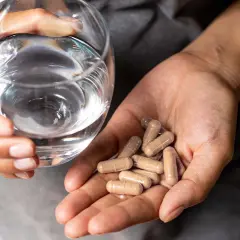 Manos sostienen un vaso de agua y cápsulas, ilustrando cómo tomar probióticos con antibióticos para el bienestar intestinal.