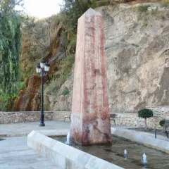 Obelisco en fuente con cascada alhama de almeria al fondo. Árboles y bancos invitan al descanso.