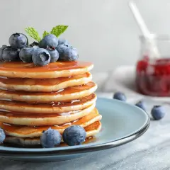 Stos puszystych naleśników polanych syropem, ozdobiony borówkami i miętą. Idealny pomysł, jak zrobić pancake na śniadanie.