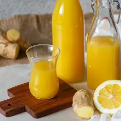 Ingwerwasser kochen oder nicht? Frischer Ingwer, Zitrone und goldgelbes Ingwerwasser in Flaschen und Glas.