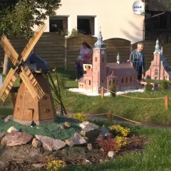 Drewniany wiatrak i kościółek w miniaturze, jakby z bajki. Strysza buda w tle, a obok ludzie podziwiający makietę.