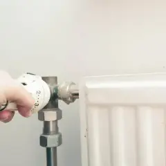 Dłoń reguluje termostat grzejnika. Po odpowietrzeniu zimny grzejnik w końcu zacznie grzać.