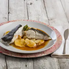 Rodaballo gallego servido con patatas y salsa, acompañado de cubiertos y servilleta sobre una mesa de madera.