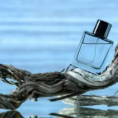 Szklana butelka perfum na dryfującym drewnie, w tle błękitna woda. Czy to zapach ambra co to?
