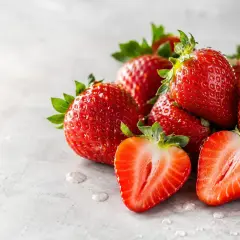 Fragole succose, ricche di potassio, su sfondo grigio. Una tagliata rivela la polpa rossa e i semini.