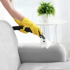 Person mit gelben Handschuhen reinigt Polstergarnitur mit einem Dampfreiniger.