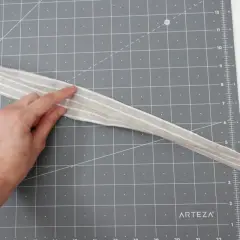 A hand points to a striped fabric strip, possibly for a belt loop pattern, on a cutting mat.
