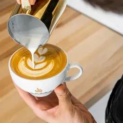 Barista tworzy latte art, wlewając spienione mleko do kawy. To świetny pomysł na to, co zamiast mleka do kawy, gdy szukasz czegoś innego.
