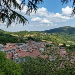 Panoramica di Montieri, Grosseto, con tetti in cotto e colline verdi sotto un cielo azzurro con nuvole bianche.