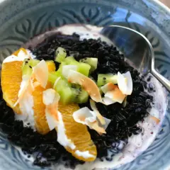 Schwarzer Reis mit Kokosmilch, garniert mit Orangenstücken, Kiwi und Kokoschips. Ein köstliches Dessert.