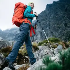 Kobieta z plecakiem i kijkami przemierza skalisty szlak. Cieszy się pięknem górskiego krajobrazu podczas wędrówki.
